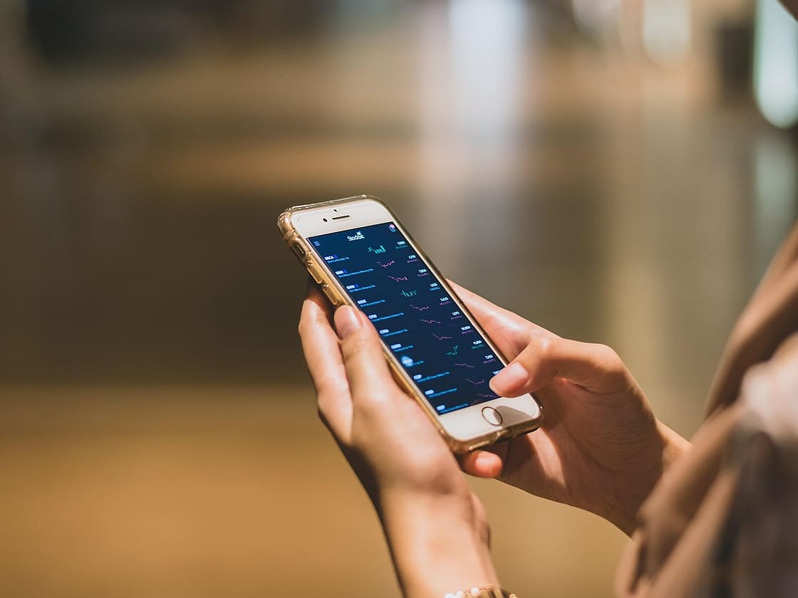 Dłonie trzymają telefon z otwartą aplikacją finansową, ciepłe rozmyte tło