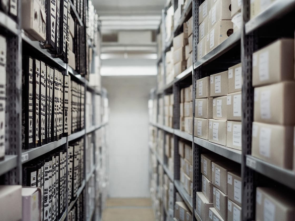 Wąski korytarz między regałami z pudłami archiwalnymi