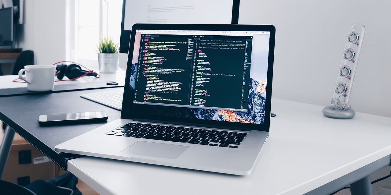 Jasne biurko przy oknie, otwarty laptop z kodem i kubek kawy