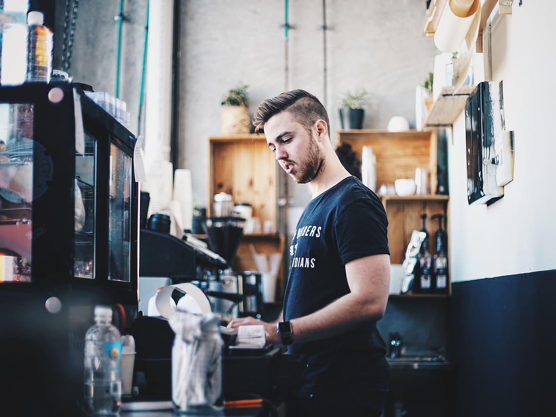 Barista przy ladzie kawiarni w jasnym wnętrzu z drewnianymi półkami